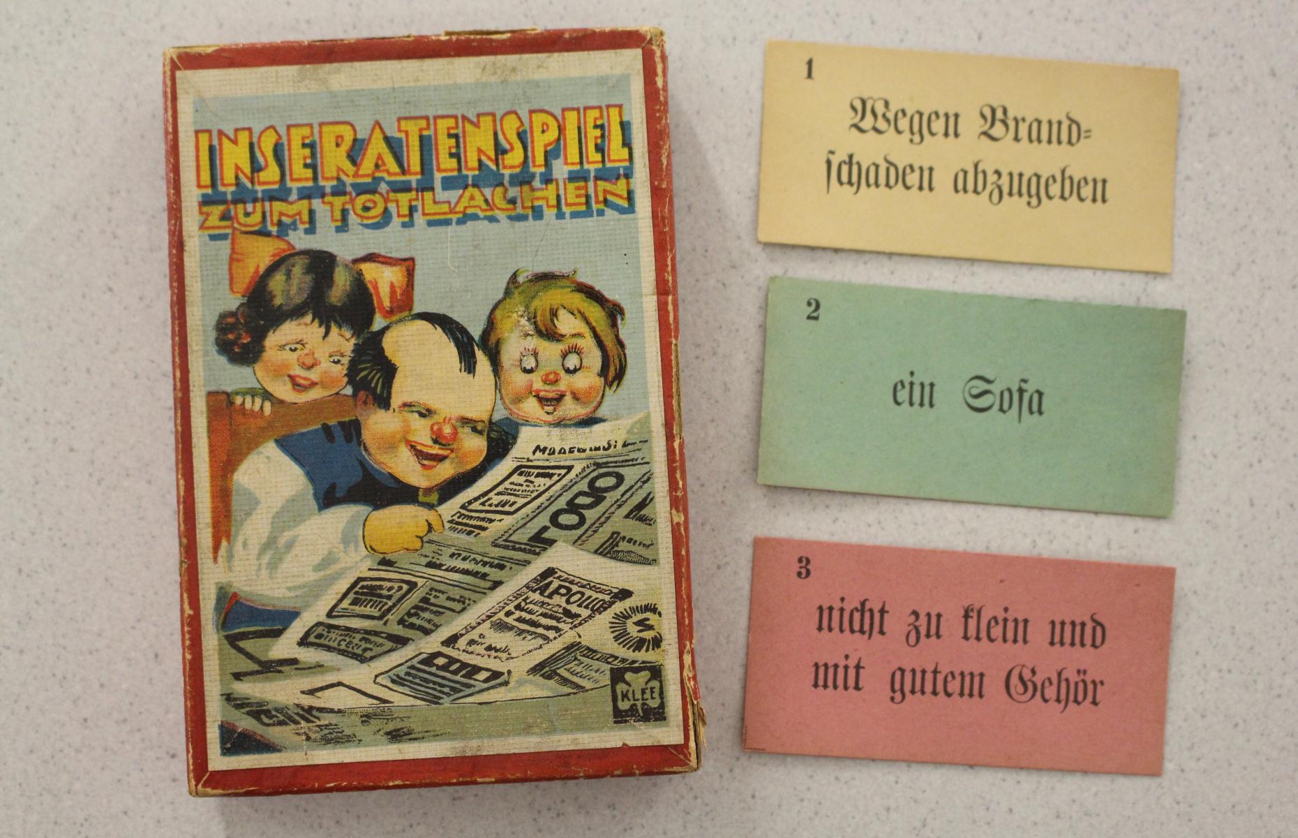 Die Schachtel des Inseratenspiels zum Totlachen mit drei der enthaltenden Spielkarten.