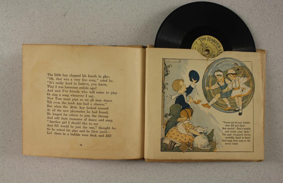 Eine Doppelseite im Buch. Auf der ersten Seite ist Text und auf der zweiten Seite befindet sich eine Illustration. Oben lugt eine Schelllackplatte heraus.